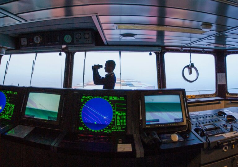 A ship officer monitoring navigation from the bridge while overseeing vessel operations at sea.