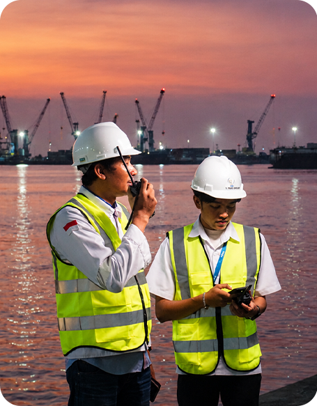 TMA GROUP personnel coordinating vessel operations using marine radio communication at an Indonesian port during sunset.